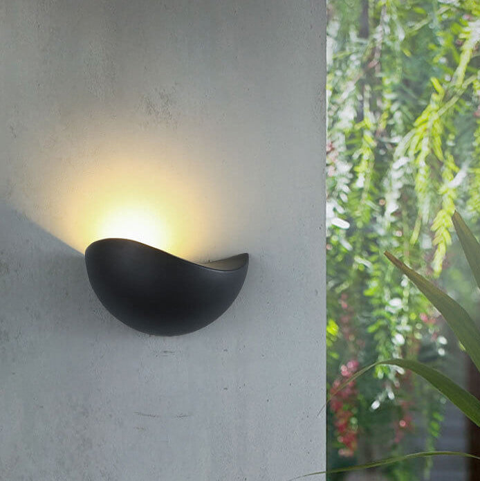 Modern outdoor wall light fixture on a concrete wall with greenery in the background