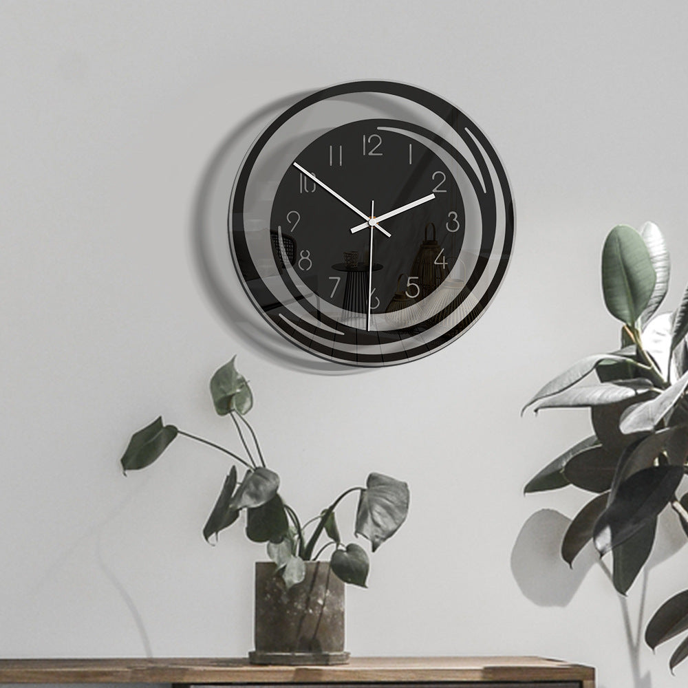 Modern wall clock with black and silver design on a white wall with plants.