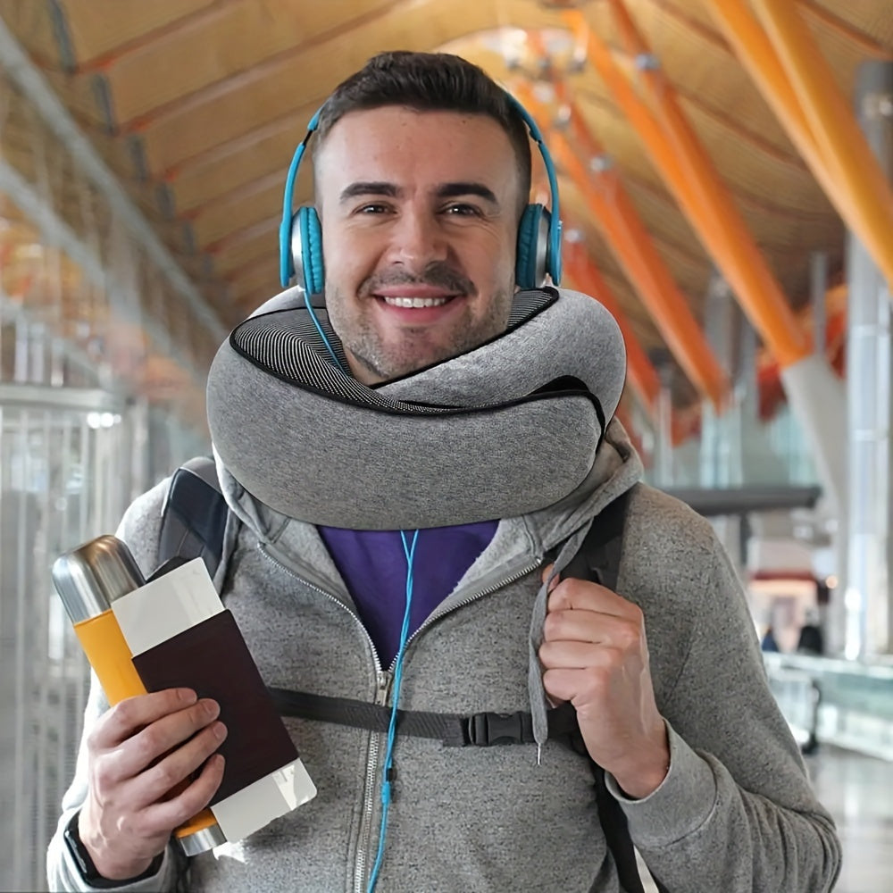 Man wearing a neck pillow, holding a travel mug and passport, in an indoor setting.