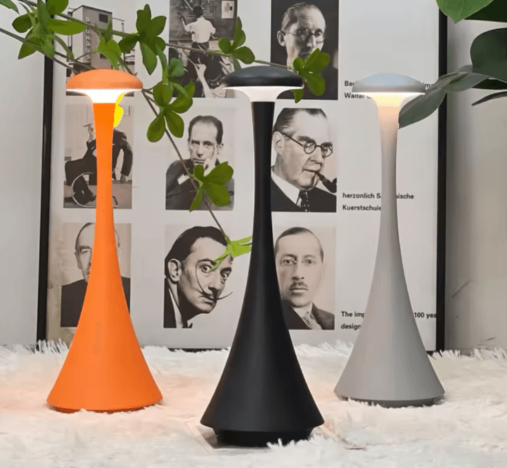 Three lamps in orange, black, and gray on a white surface with a collage of black and white portraits in the background.