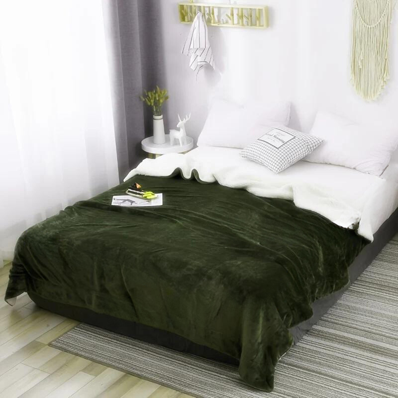 Bed with green blanket and white pillows in a room with a small table and plant.