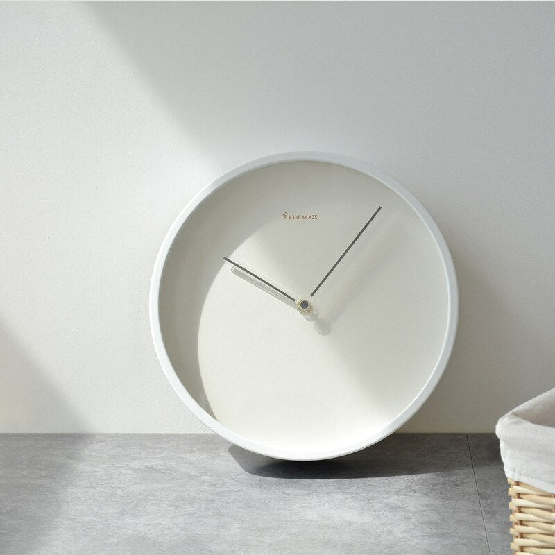 White wall clock on a light gray wall with a basket in the corner