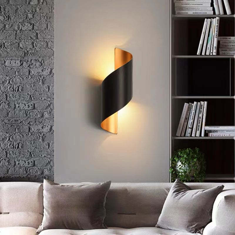 Modern wall sconce on a wall next to a bookshelf with a sofa and decorative pillows.