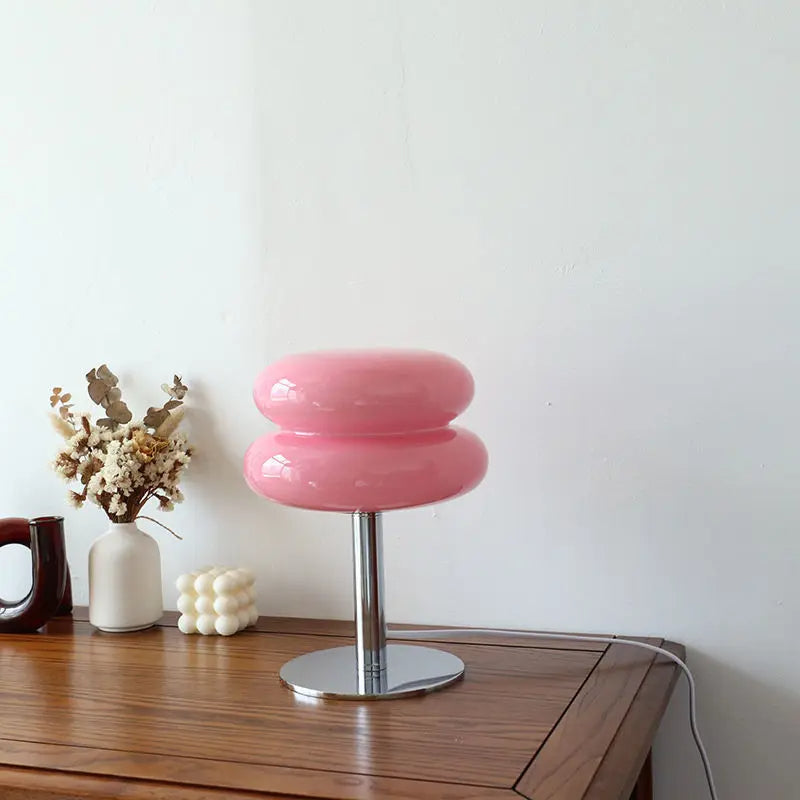 Pink stool with a metallic base on a wooden surface against a white wall
