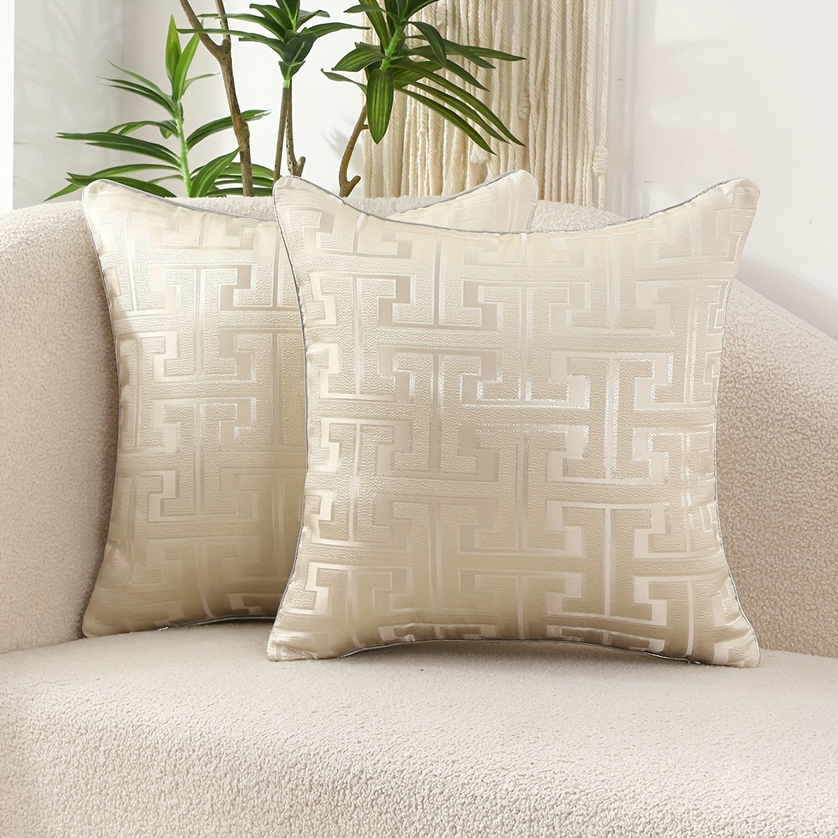 Two patterned pillows on a beige couch with a plant in the background