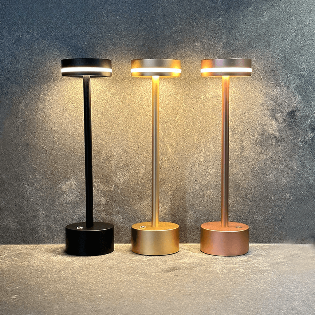 Three standing lamps in black, gold, and bronze on a textured surface with a gray background.