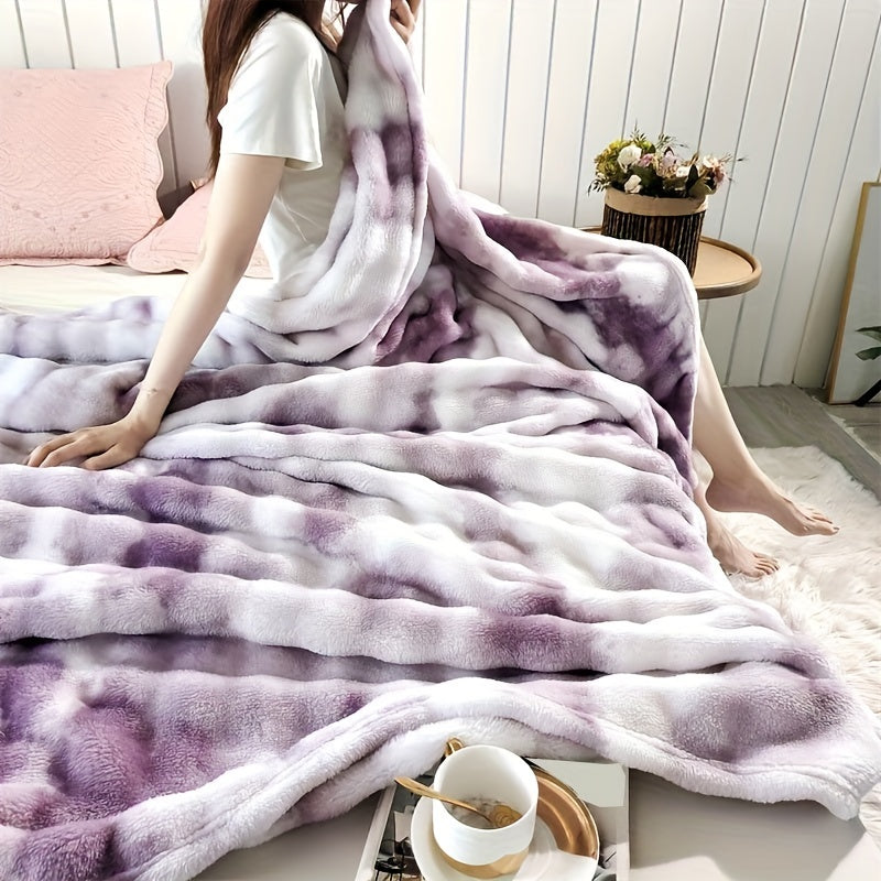 Person sitting on a bed covered with a purple and white tie-dye blanket in a cozy bedroom setting.