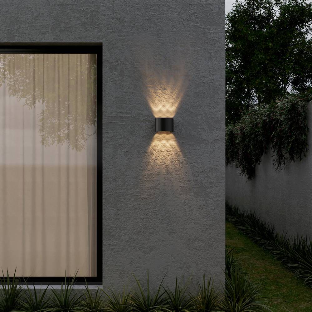 Wall-mounted outdoor light fixture on a gray wall with a window and garden in the background