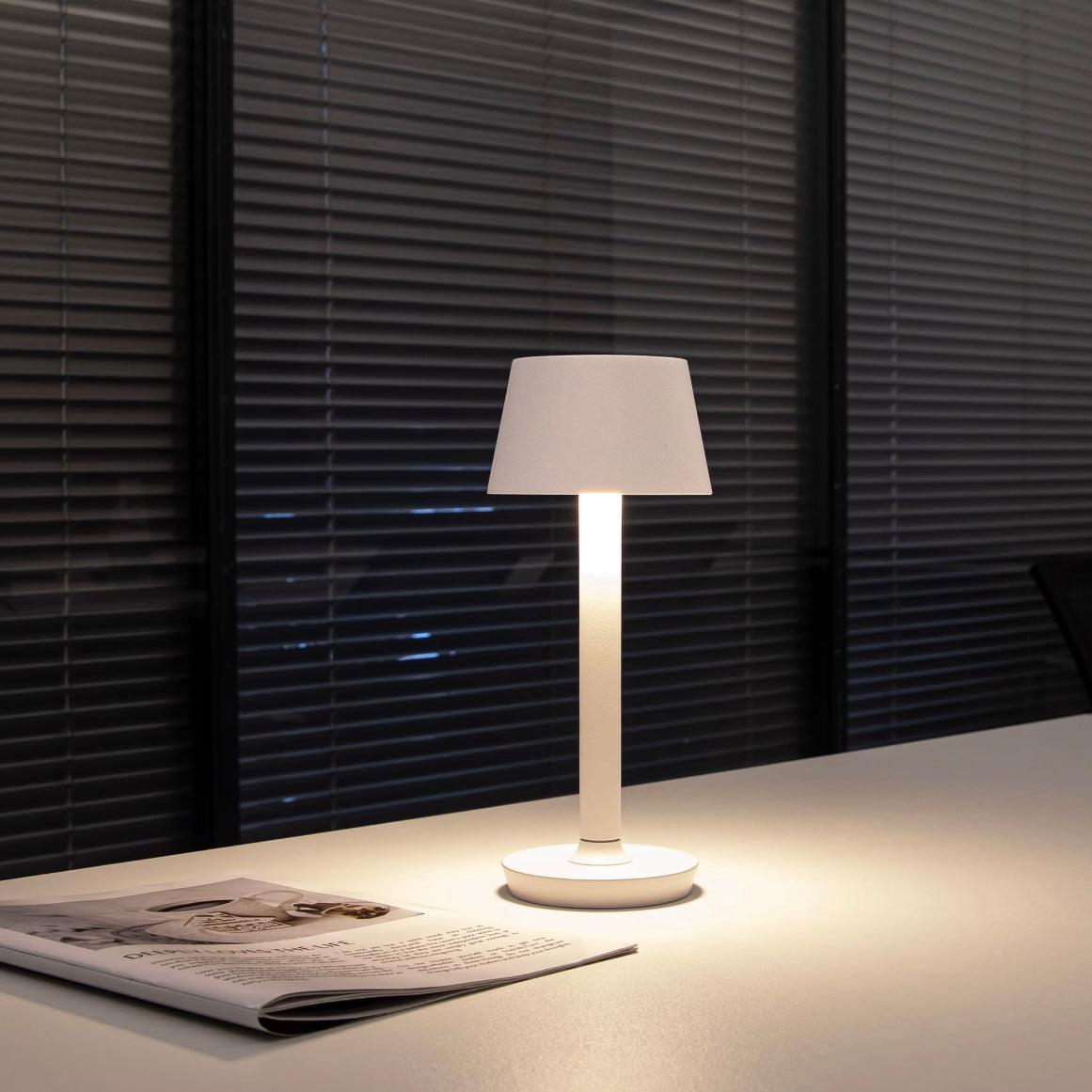 Table lamp on a surface with a newspaper in front of a window with blinds.