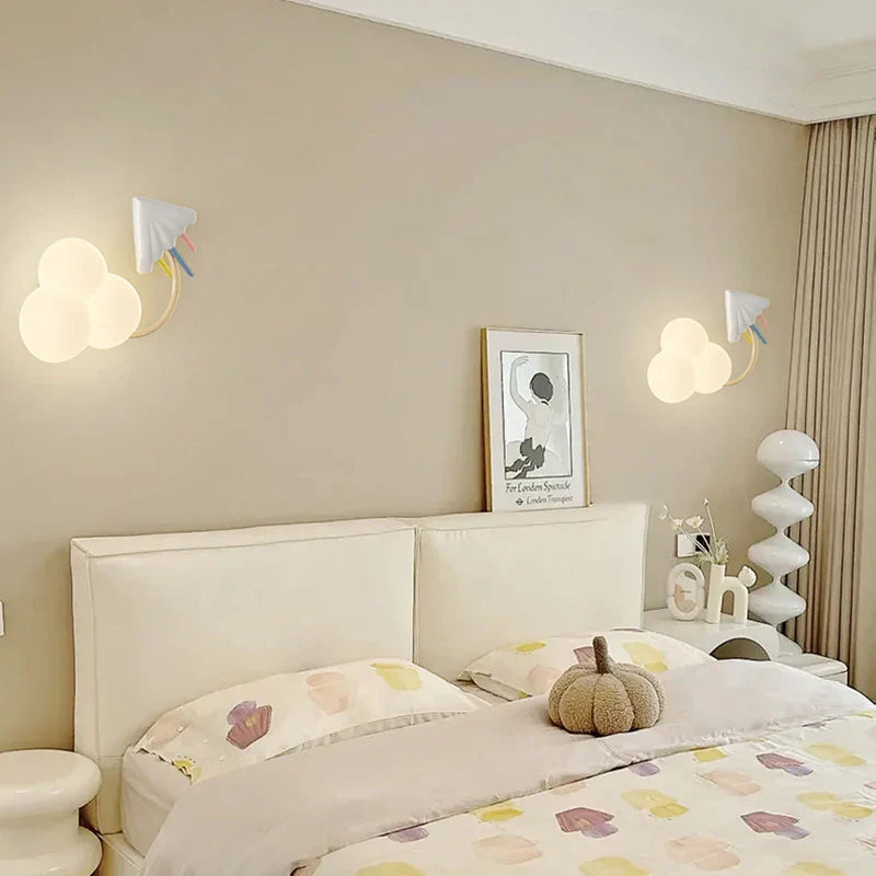 Neatly made bed in a bedroom with decorative pillows and a pumpkin, featuring wall lights and a framed picture.