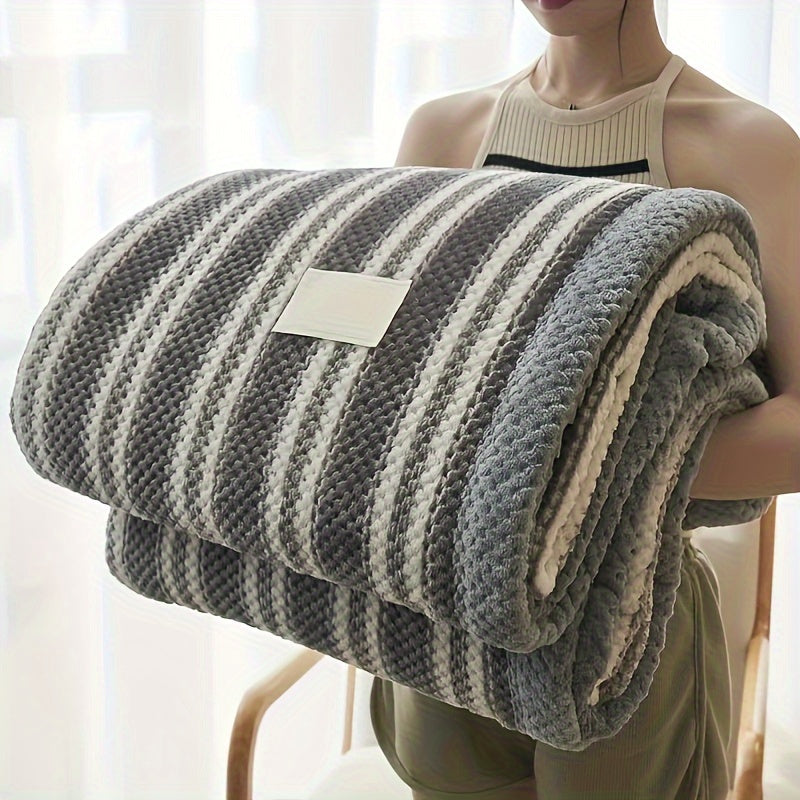 Person holding a striped blanket with a visible brand tag in a bright room.