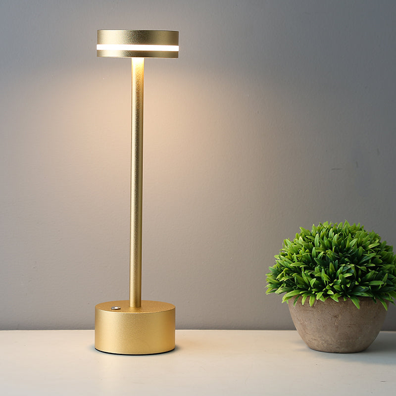 Gold table lamp on a gray surface with a plant in the background