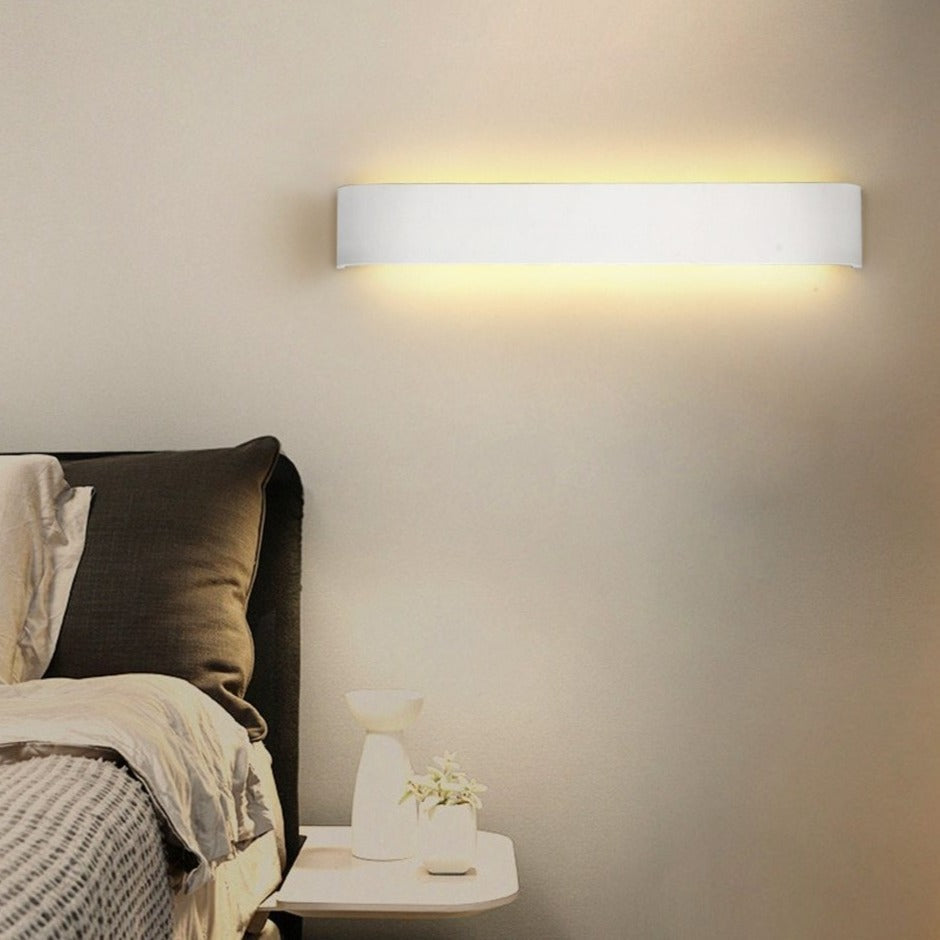 Wall-mounted light fixture on a bedroom wall with a bed and side table in the foreground.