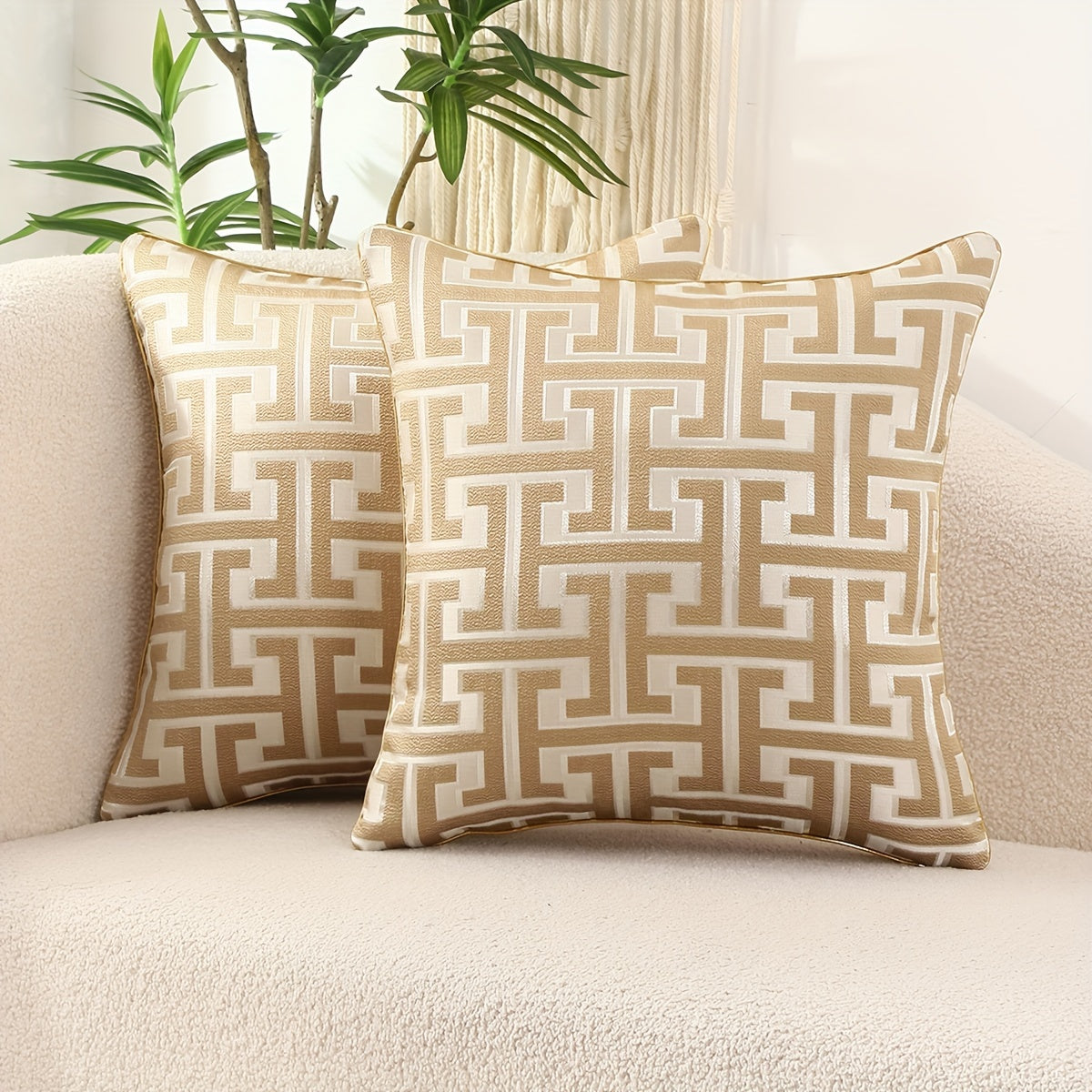 Two patterned pillows on a beige sofa with a plant in the background