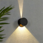 Modern black wall light fixture casting a shadow on a textured wall with a plant leaf in the corner.