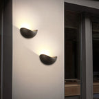Two modern wall lights on a white wall with a dark interior setting.