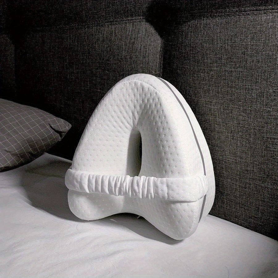 White U-shaped pillow on a bed with a dark gray couch in the background