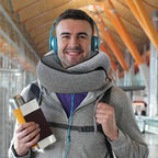 Man wearing a neck pillow, holding a travel mug and passport, in an indoor setting.