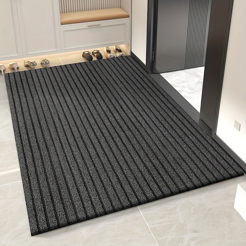 Textured black doormat on a tiled floor with shoes in the background