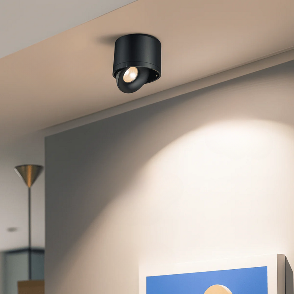 Black ceiling light fixture on a beige ceiling with a soft glow on the wall.