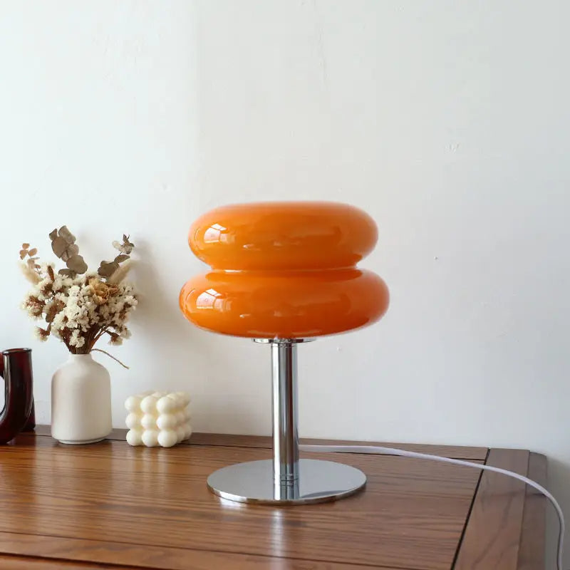 Orange table lamp with a white cord on a wooden surface with decorative items.