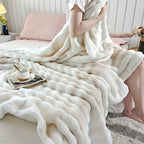 Person wrapped in a fluffy white blanket on a bed with a cup and saucer on a small table.