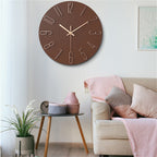Brown wall clock on a white wall above a beige sofa with pink and gray cushions.