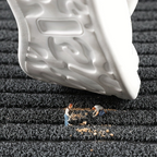Close-up of a white shoe sole on a textured black surface with small figures working on it.