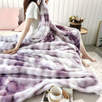 Person sitting on a bed covered with a purple and white tie-dye blanket in a cozy bedroom setting.