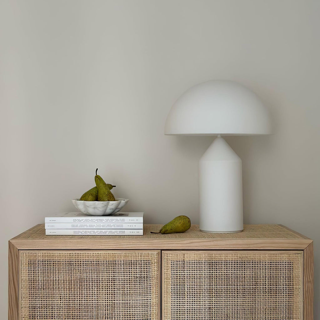 White lamp on a wooden cabinet with books and pears against a plain wall
