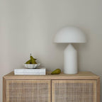 White lamp on a wooden cabinet with books and pears against a plain wall
