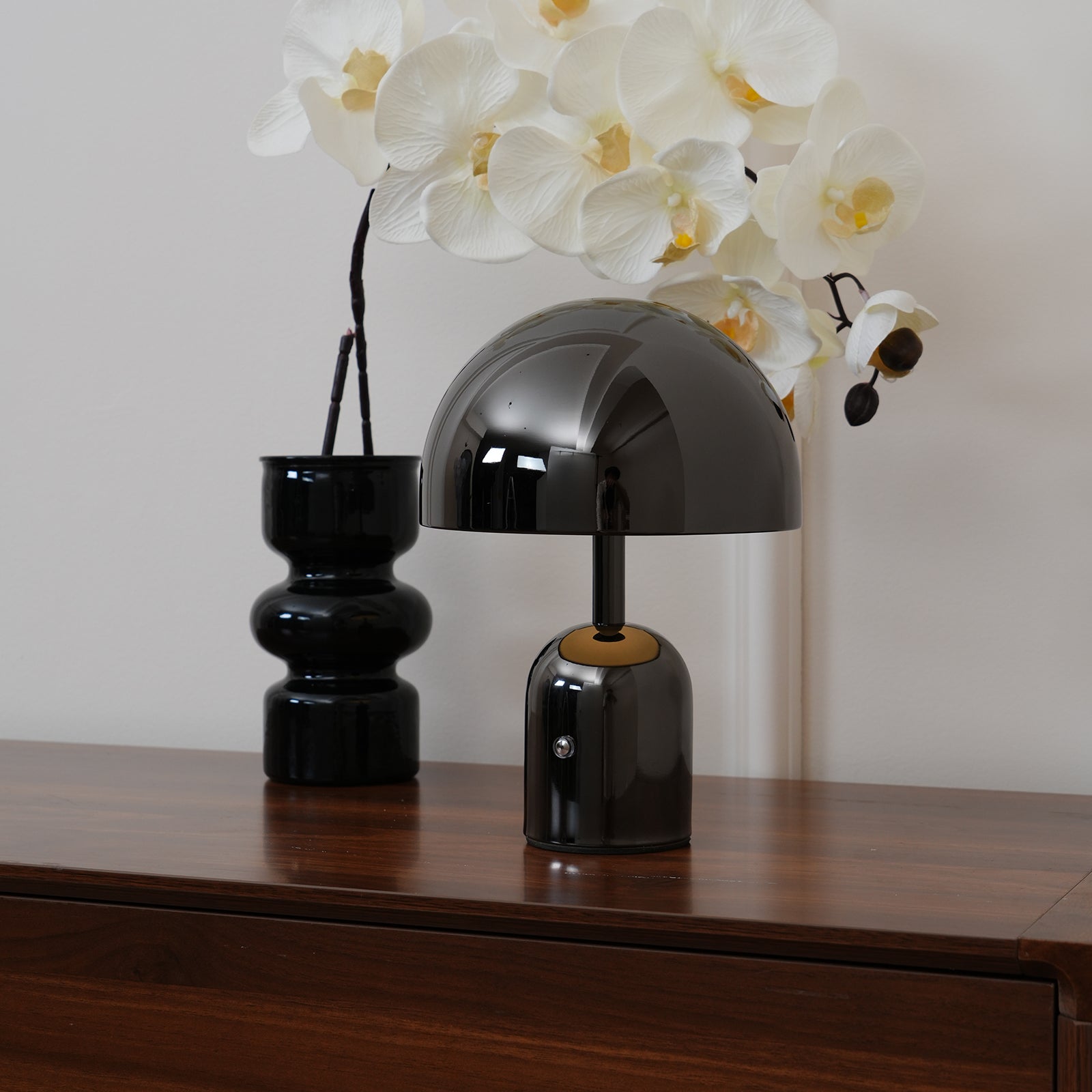 Black lamp and vase on a wooden surface with white flowers in the background
