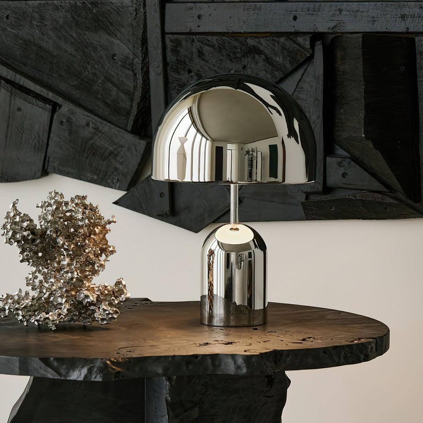 Chrome table lamp on a wooden table with a decorative plant in the background.