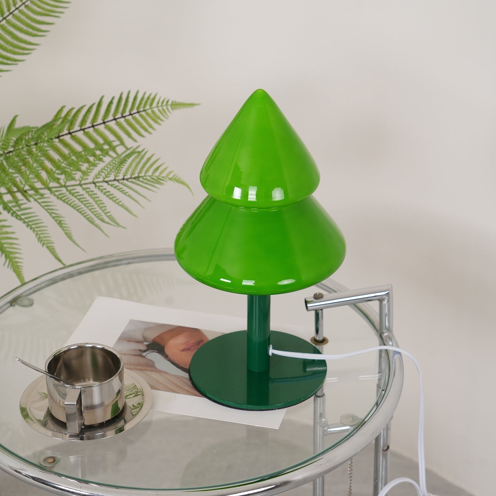 Green tree-shaped lamp on a glass table with a plant in the background