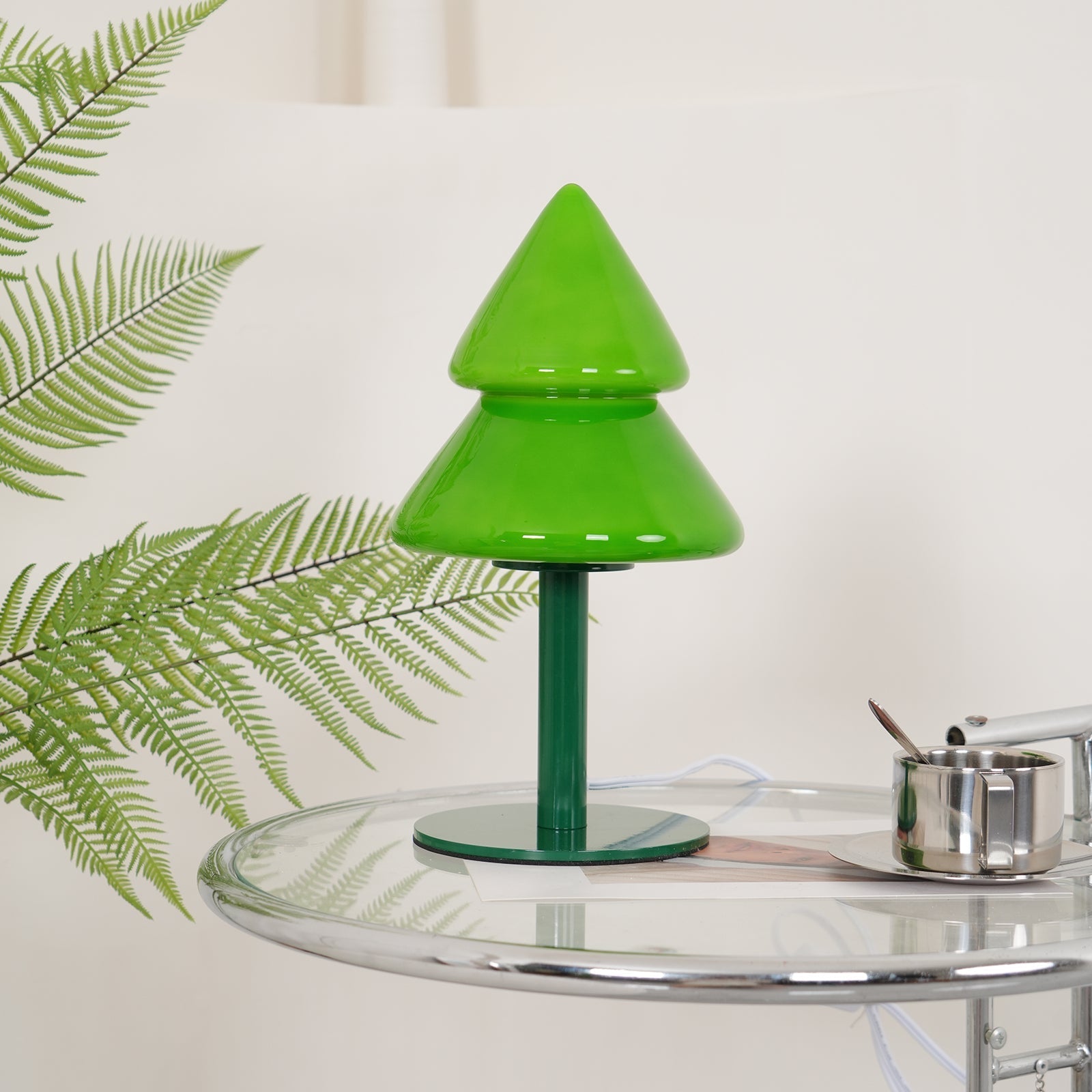 Green table lamp on a glass surface with a leafy plant in the background