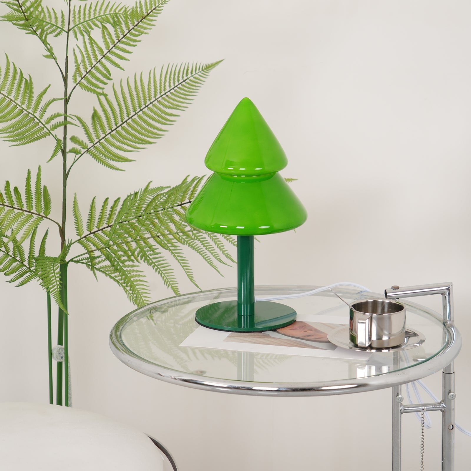 Green lamp on a glass table with a plant in the background