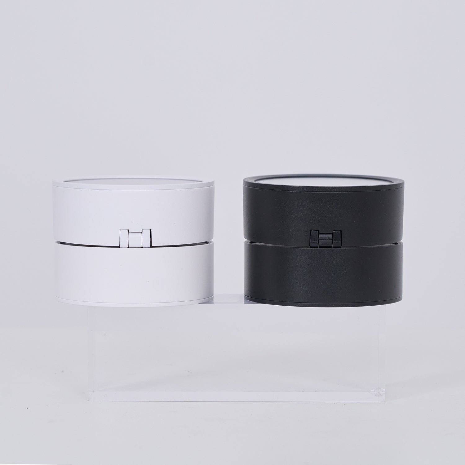 Two cylindrical lamp, one white and one black, on a light gray background.