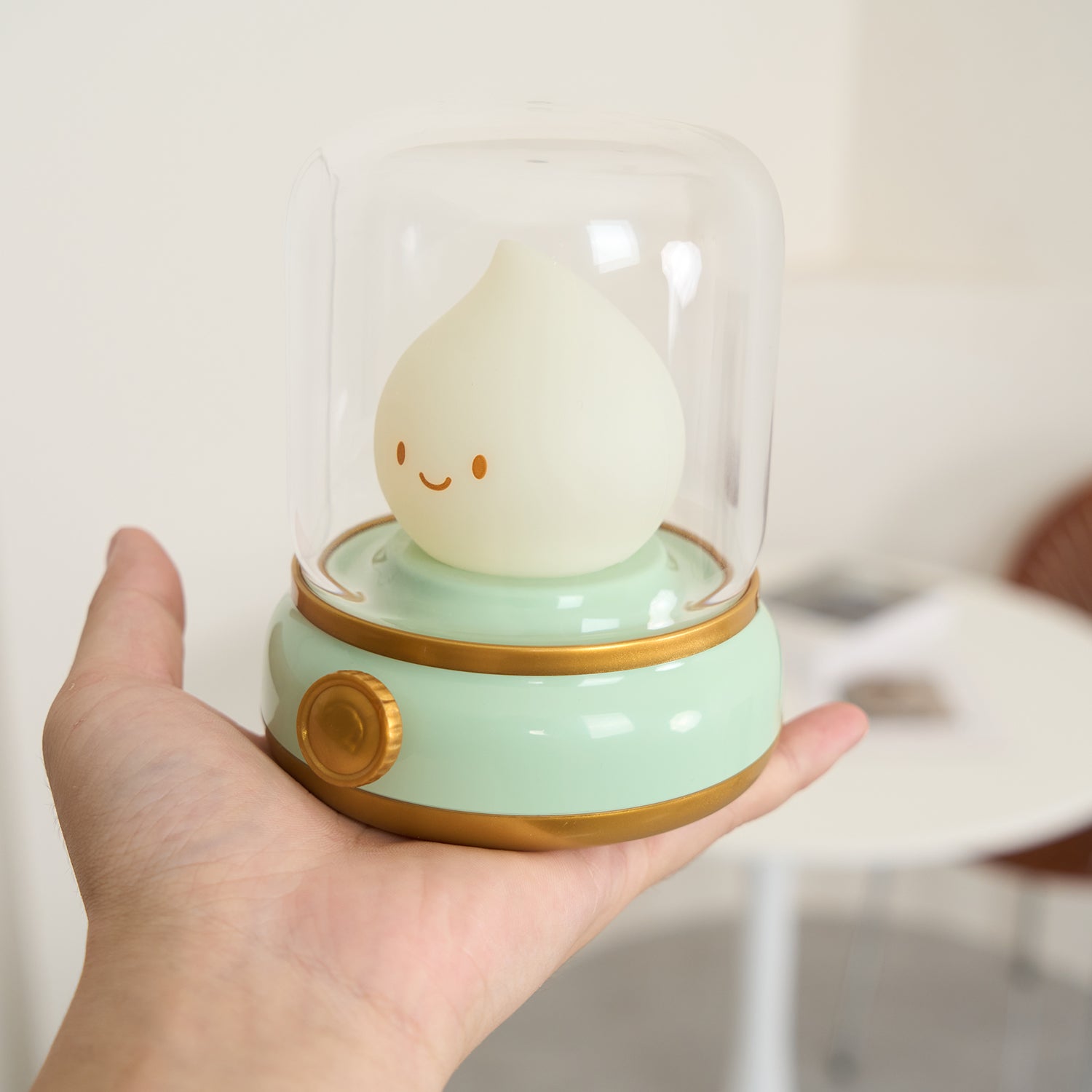 Small lamp with a smiling face inside a glass dome held in a hand against a blurred background