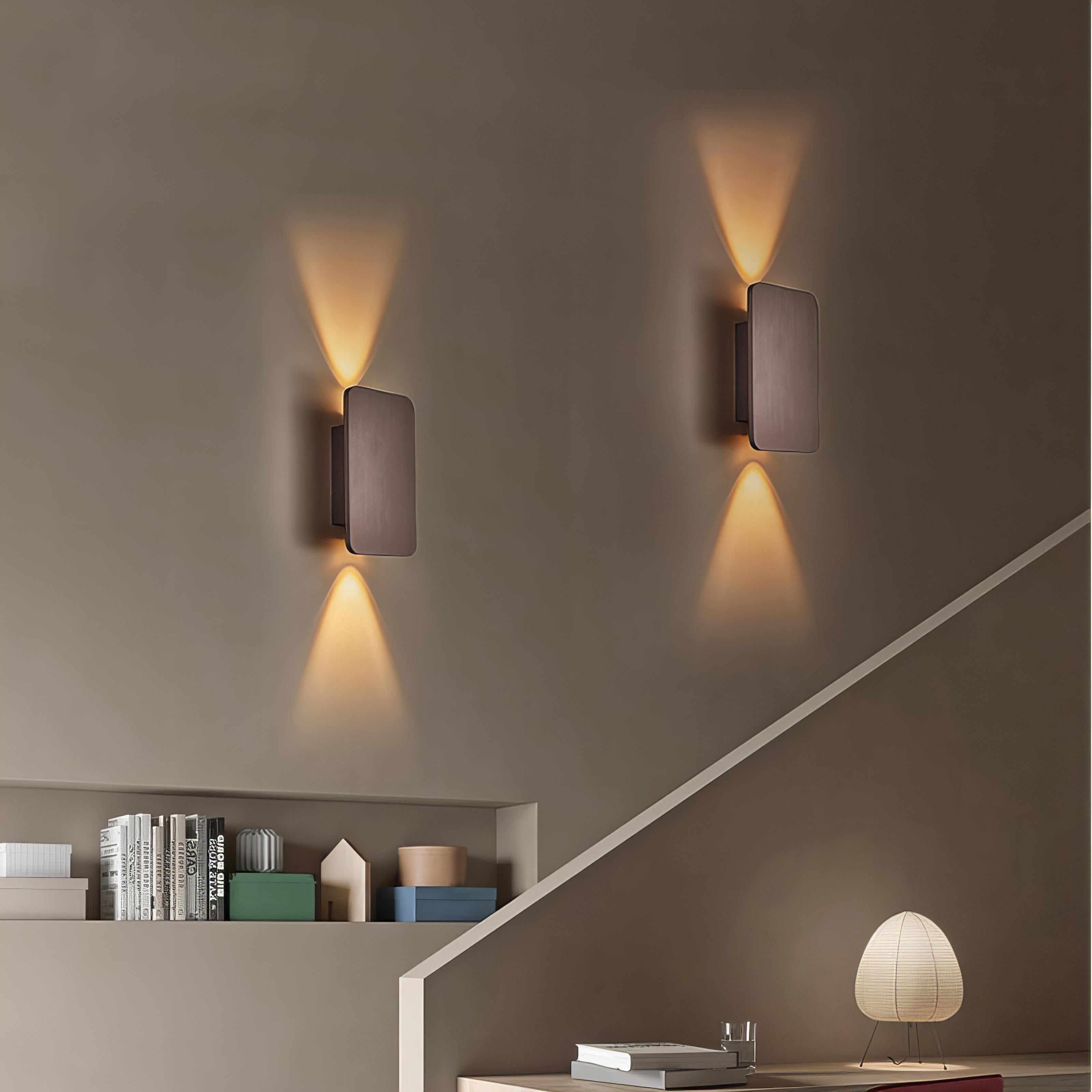 Two wall-mounted square lights casting shadows on a wall with a shelf below.