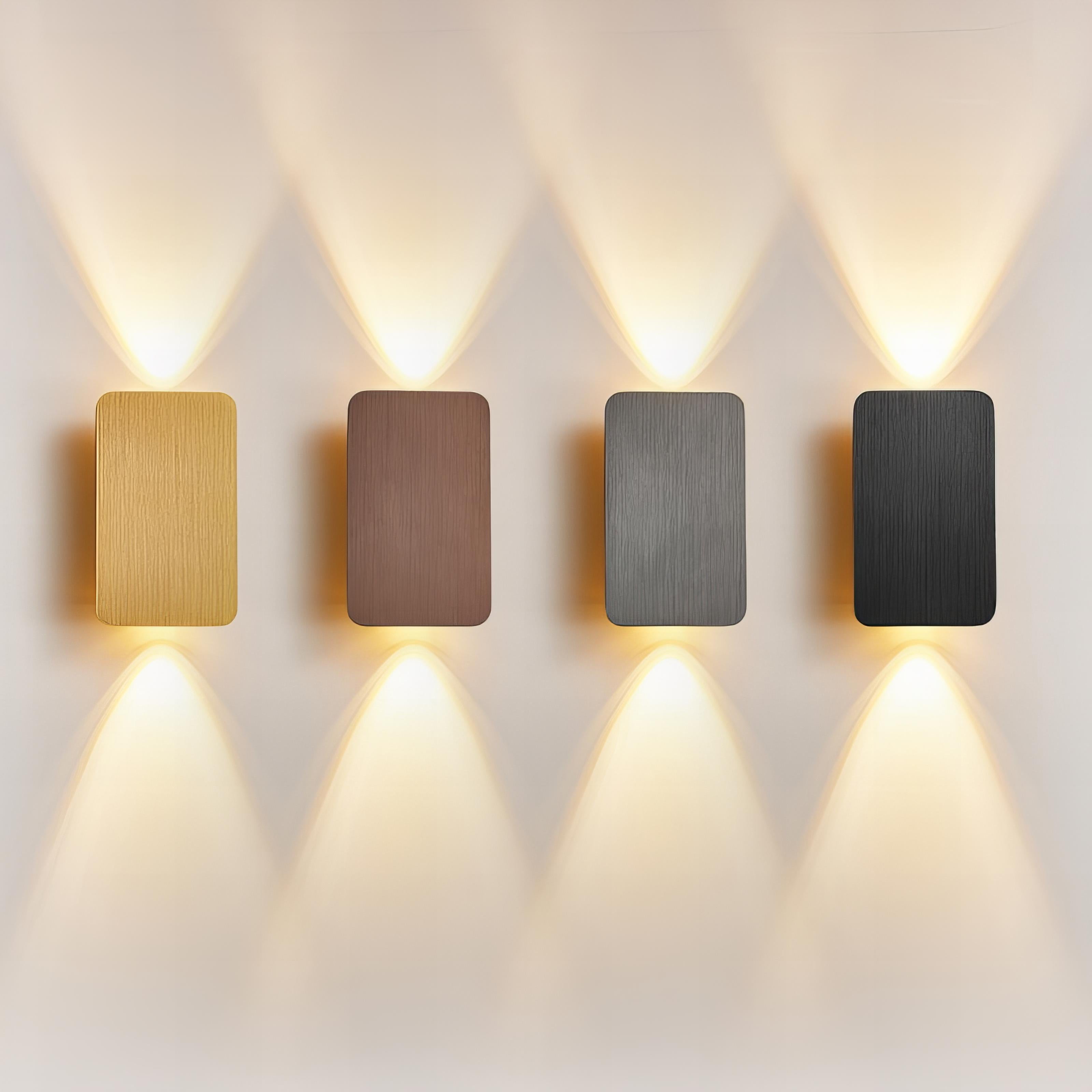 Four rectangular wall lights in gold, bronze, silver, and black on a white wall.