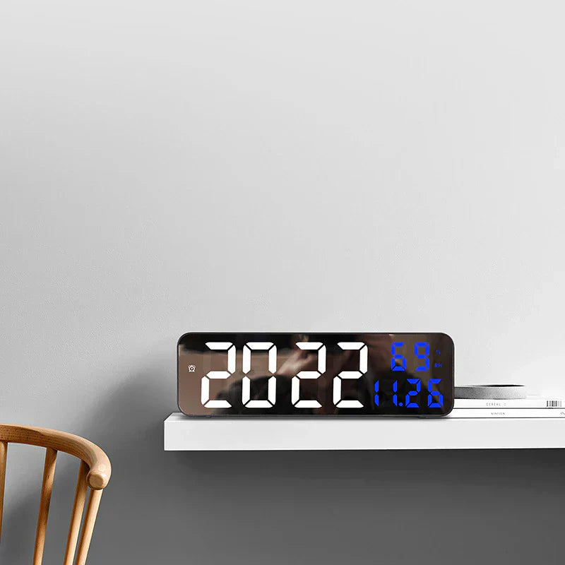 Digital clock on a white shelf against a gray wall