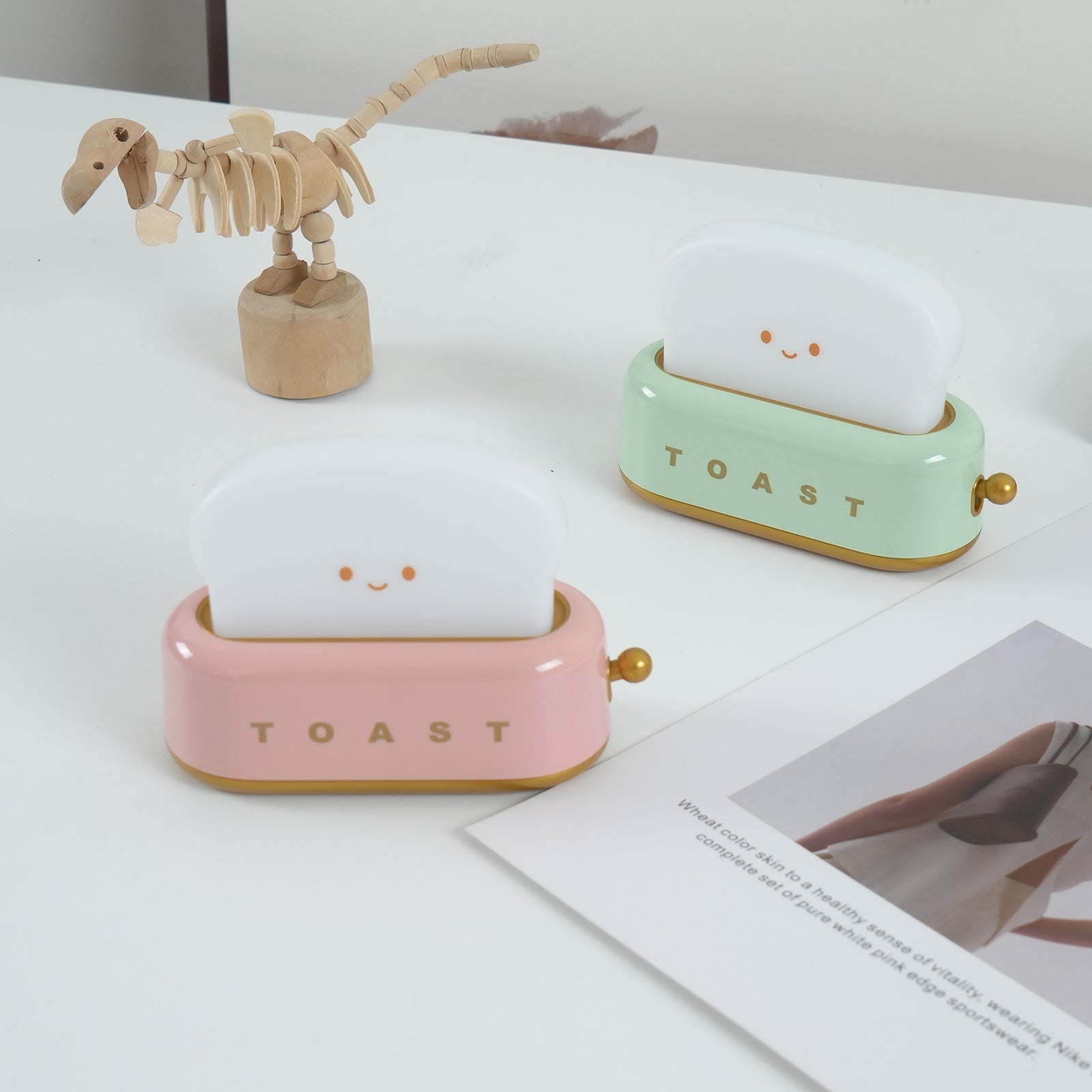 Two small ceramic toast-shaped lamps on a surface with a wooden skeleton toy.