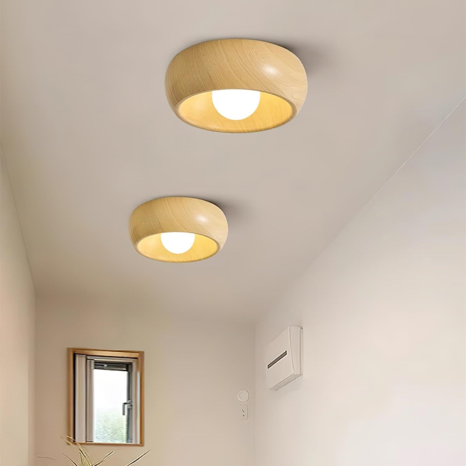 Two wooden ceiling lights on a white ceiling with a small window and plant in the background.