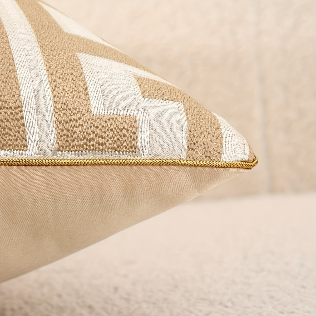 Close-up of a beige pillow with white stripes and a gold trim on a beige background.