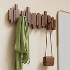 Wooden wall hook with a green scarf and brown handbag on a beige wall.