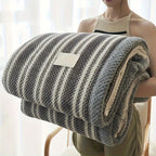 Person holding a striped blanket with a visible brand tag in a bright room.