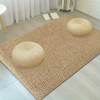 Beige woven rug with two round straw pillows on a light wooden floor.