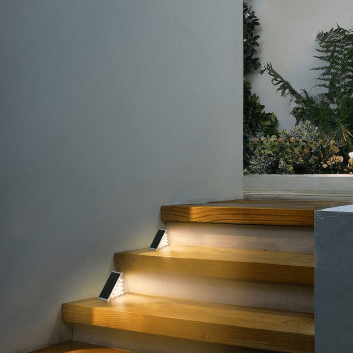 Wooden staircase with solar lights on a gray wall with plants in the background