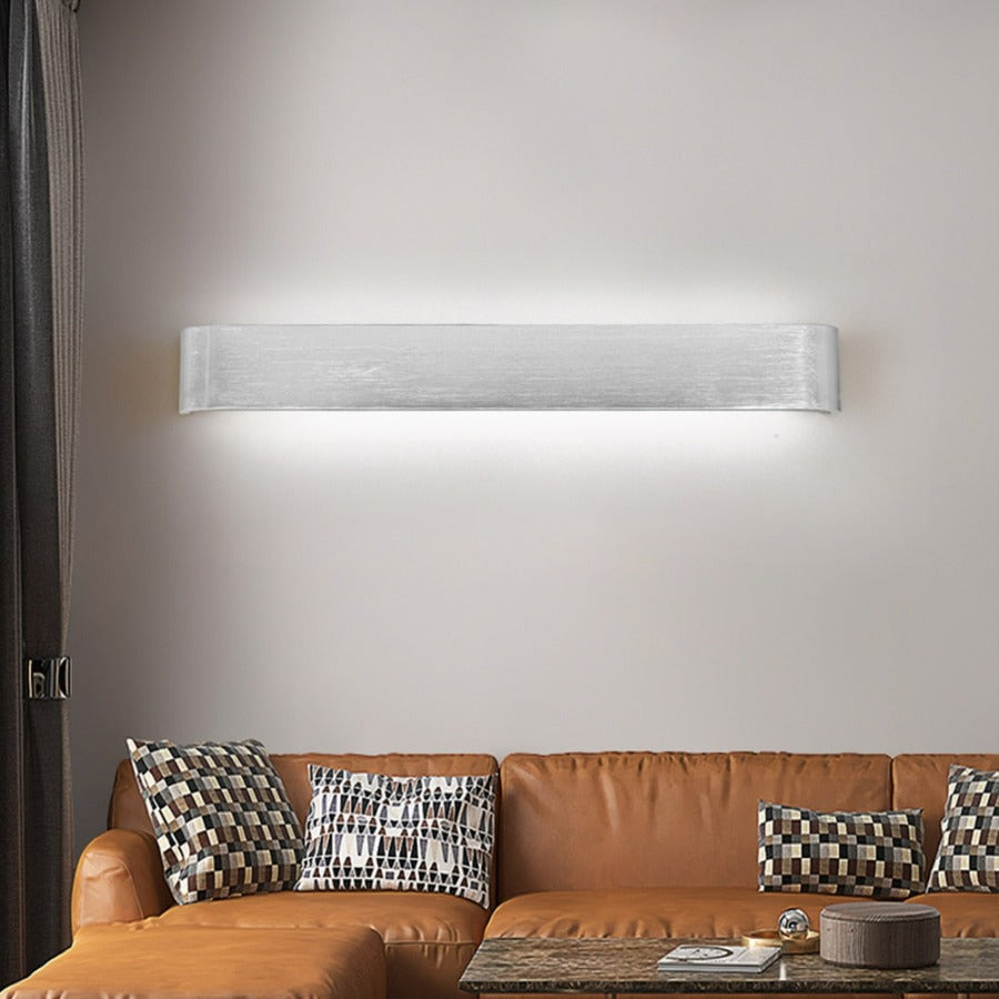 Modern wall-mounted light fixture above a brown leather sofa with patterned cushions.